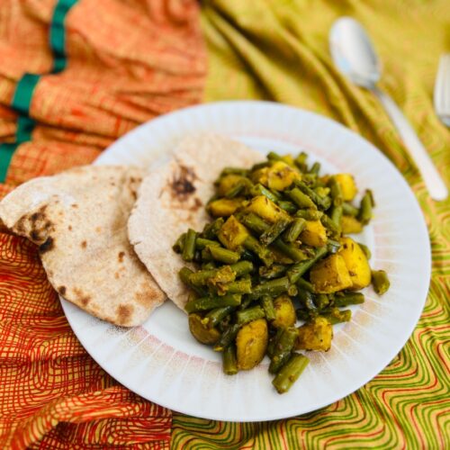 Sperziebonen en aardappel curry op een bordje met platbrood.